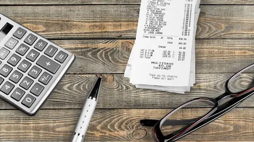 still life photo of a calculator, pen, receipts, and eyeglasses sitting on a wooden table