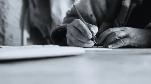 Wide low angle view of an elderly man doing calligraphy writing using a nib pen and ink