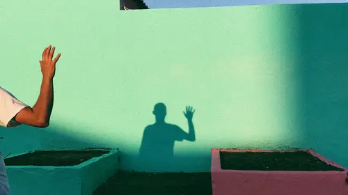 Shadow of a person saying goodbye on a green wall outdoors