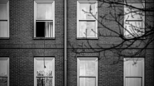 Black and white photograph of a brick building with an open window that has an extension cord hanging out of it.